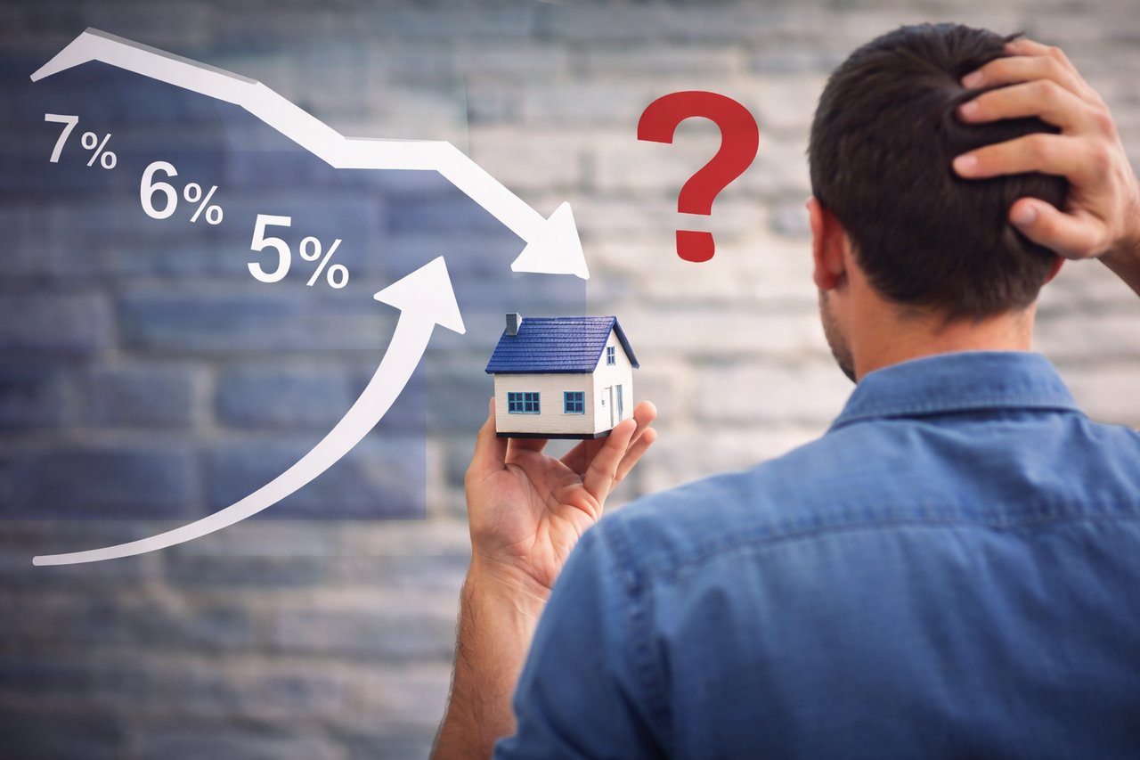 Homebuyer holding a small house while reviewing changing mortgage rate percentages