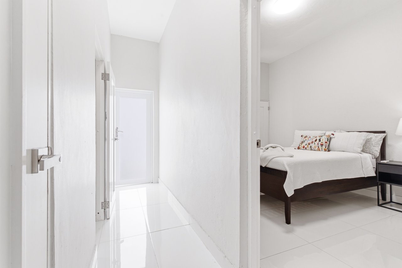 Hallway opening into a bedroom with a dark wood bed and colorful accent pillows.