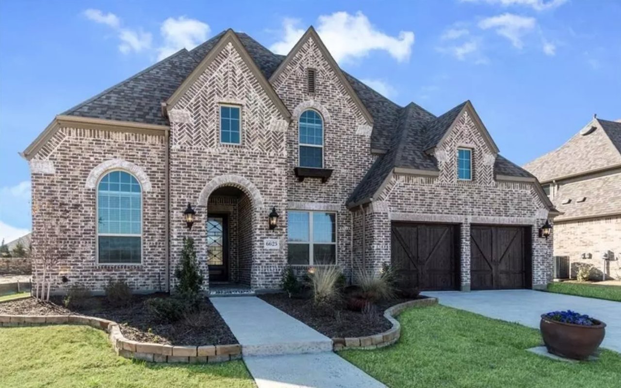Two-story brick house with arched windows, twin garage doors, and landscaped front yard.