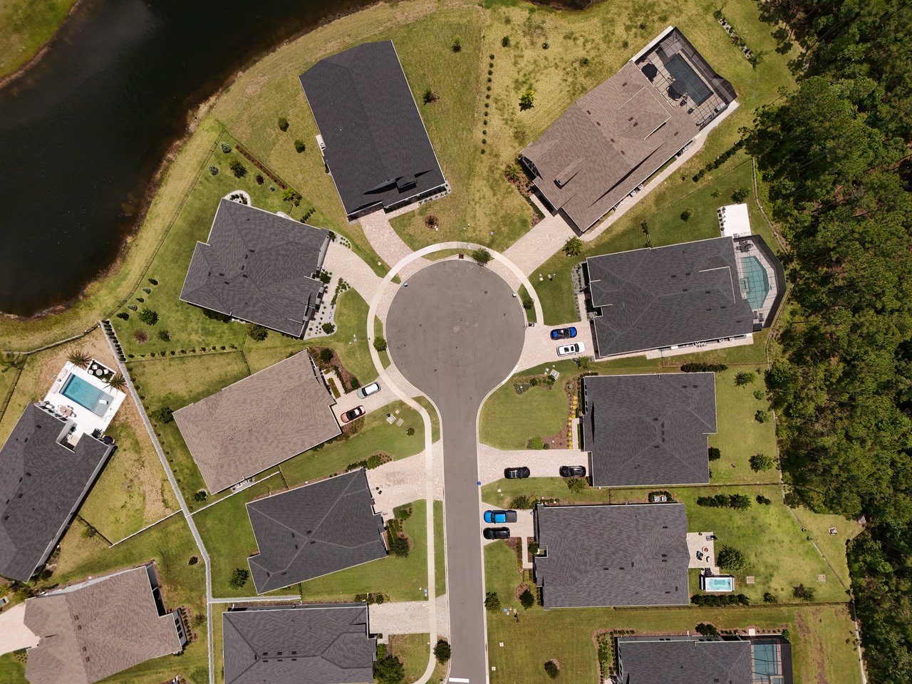 Aerial view of homes around a cul-de-sac beside a waterway, with several backyard pools.