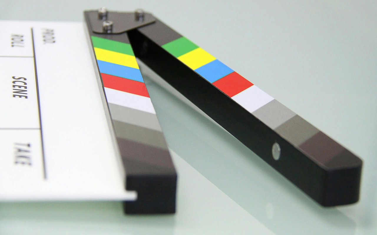 A close-up of a film clapperboard resting on a reflective surface, with its hinged sticks slightly open.