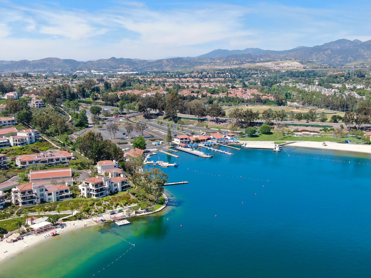 Aerial view of a coastal neighborhood, marina, and blue water with mountains in the distance.
