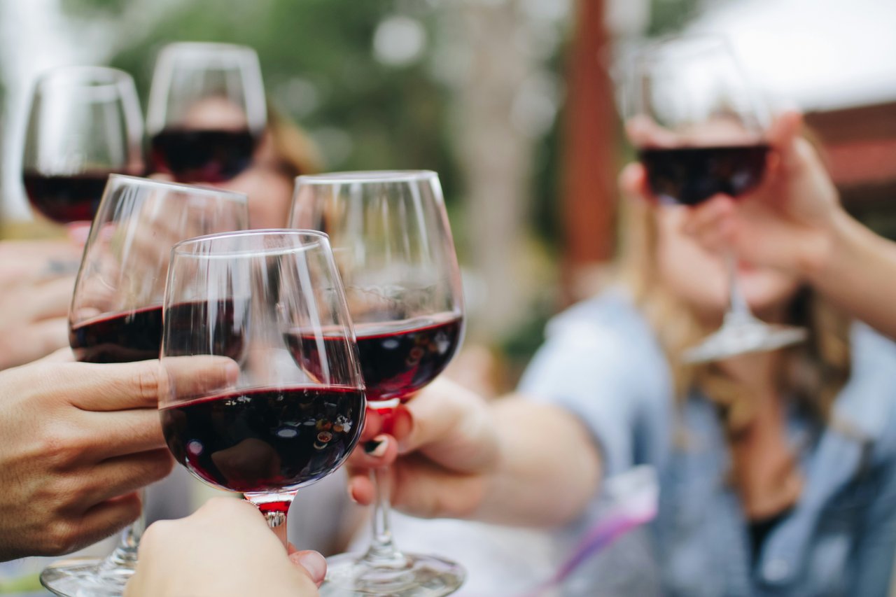 Several people toast with glasses of red wine outdoors.
