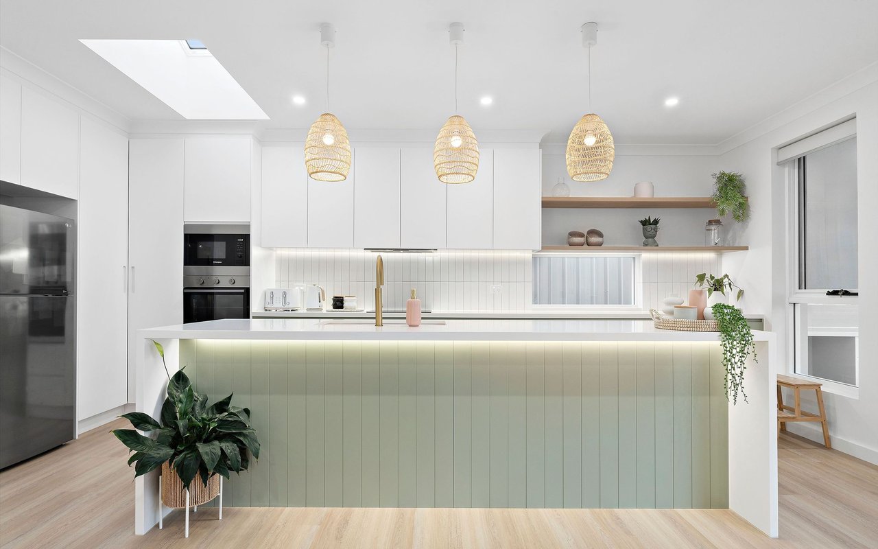 Modern white kitchen with a pale green island, gold faucet, and three woven pendant lights.