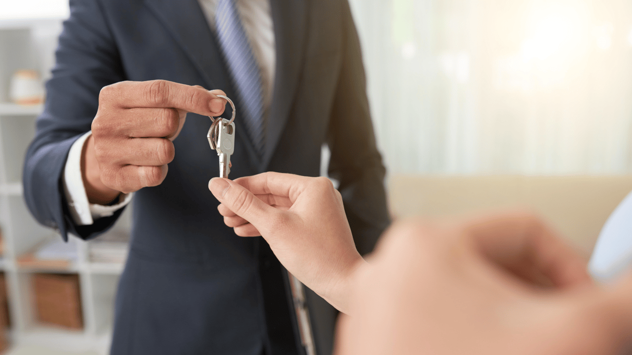 A suited agent hands a set of keys to another person in a bright office.