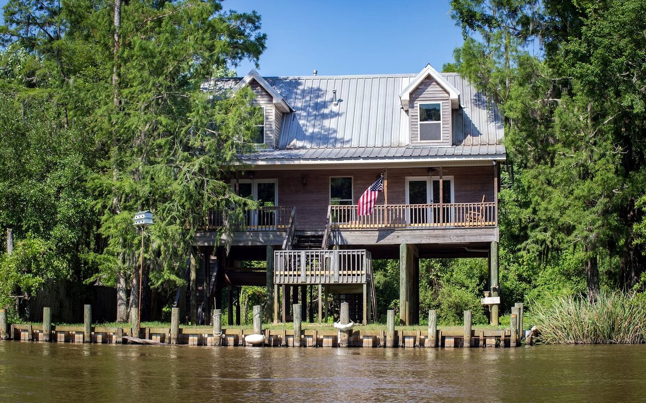 Raised waterfront home with a metal roof and broad porch above a wooden dock.