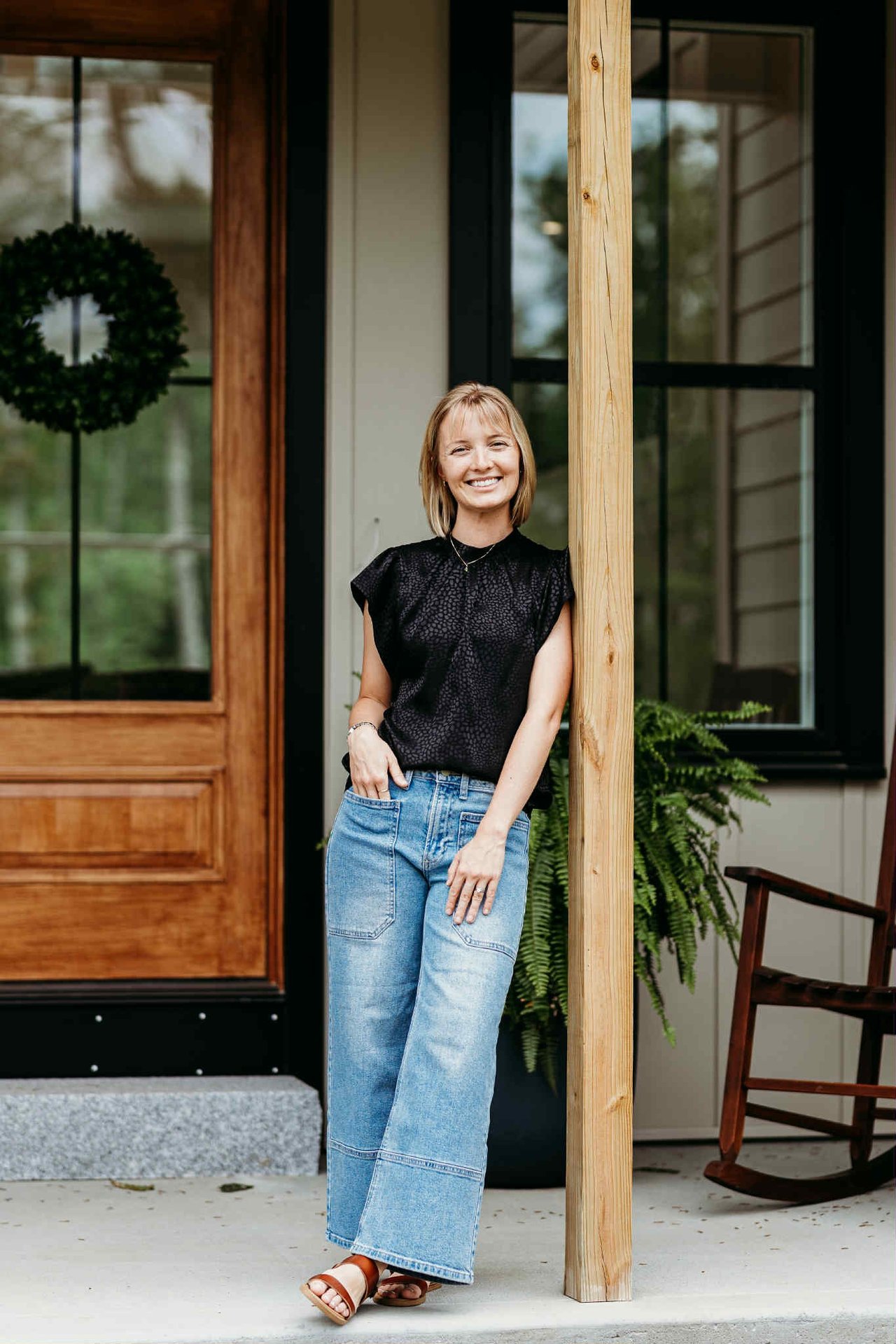 Heather Crosby smiling on a home’s porch beside a wooden post.