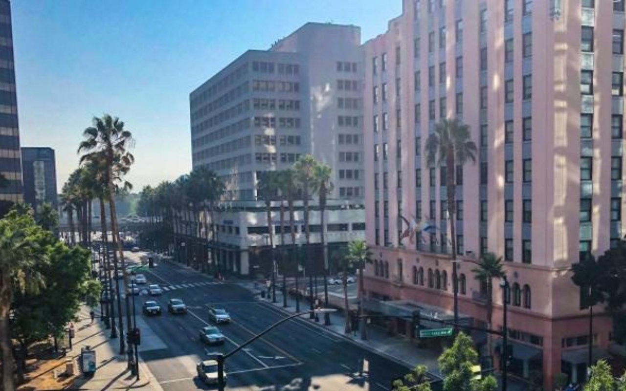 Downtown street with palm trees, tall buildings, and cars at an intersection.