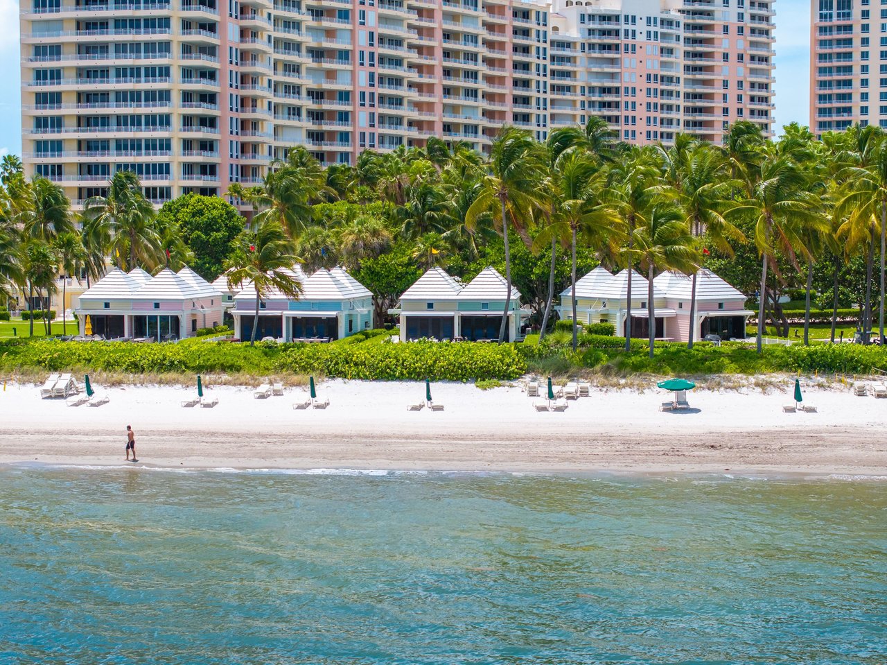 Beachfront cabanas at The Ocean Club, backed by palm trees and high-rise buildings along the shore.