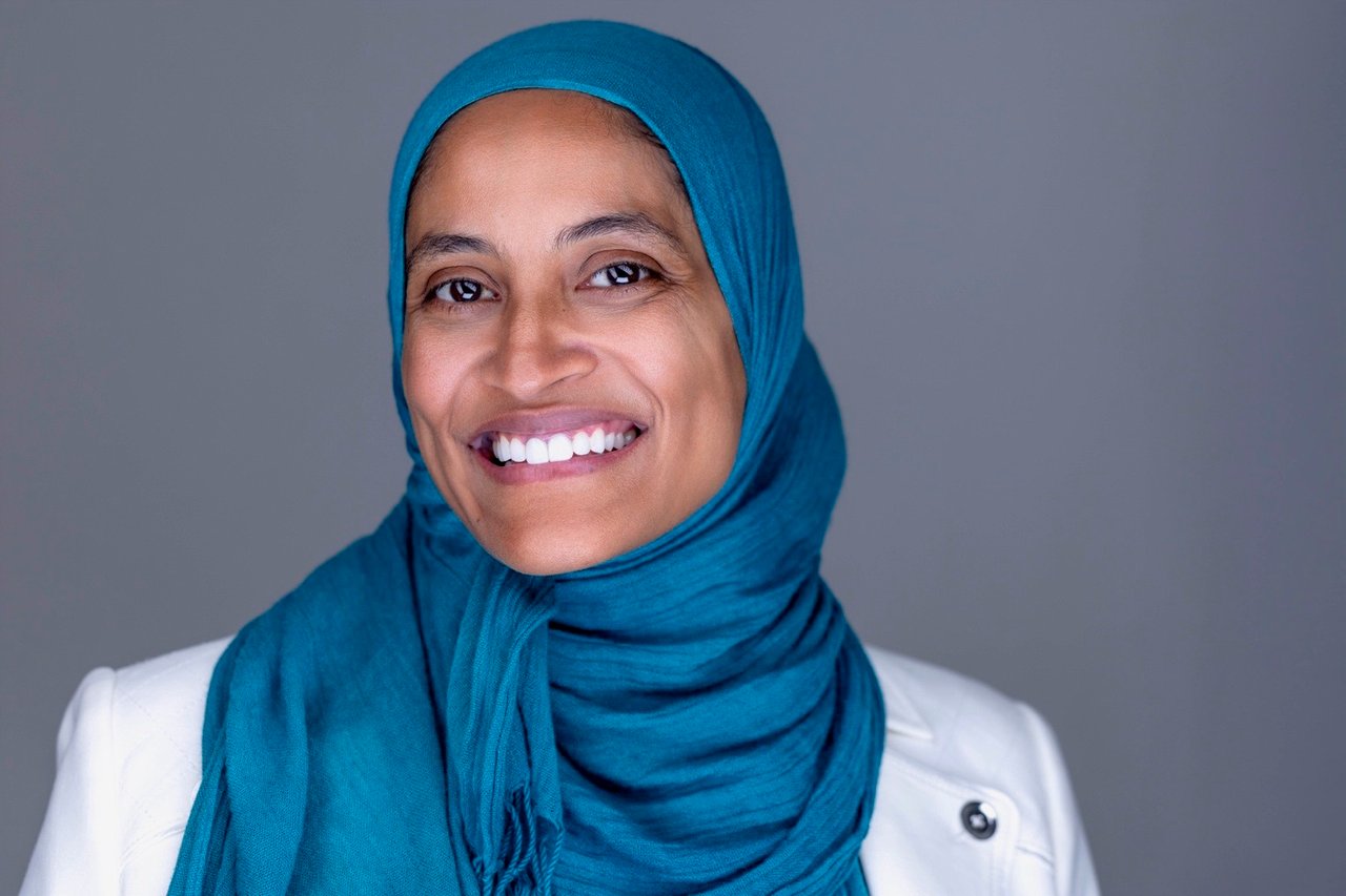 Khedija Khiyar smiling in a teal hijab and white blazer.