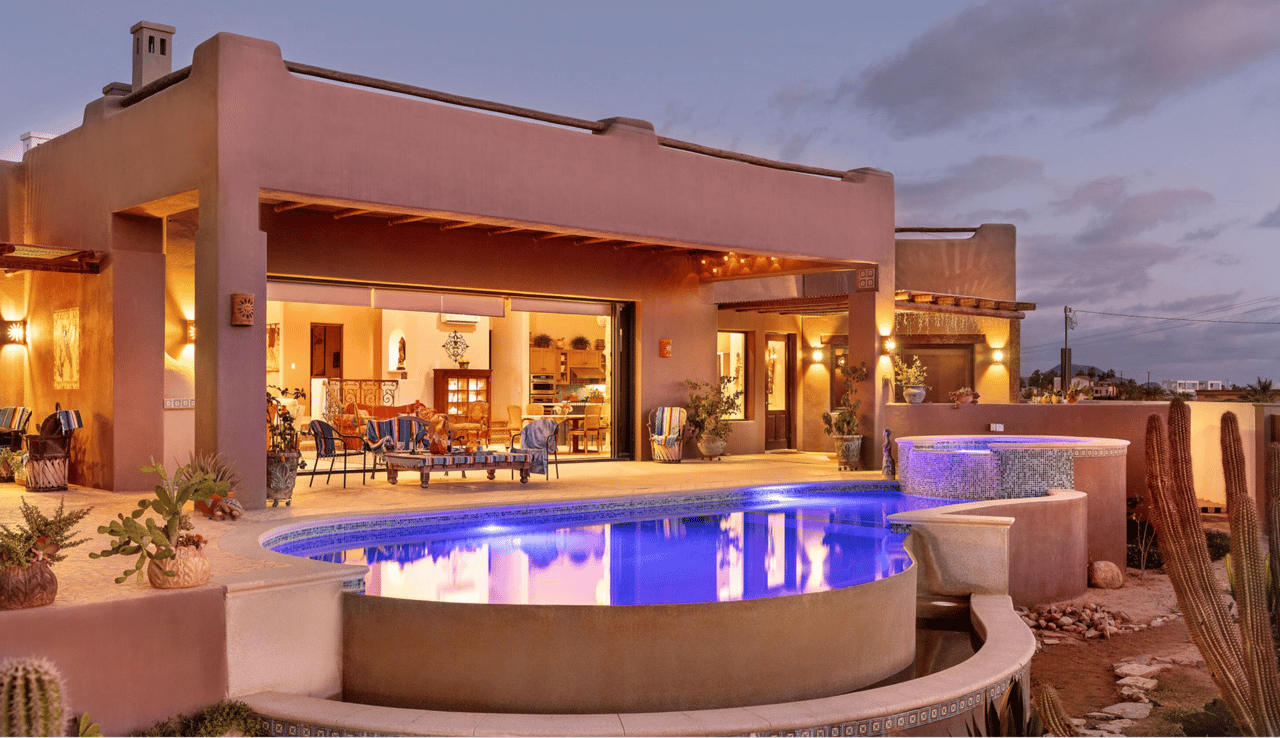 Stucco home with a curved pool and raised spa glowing at dusk.