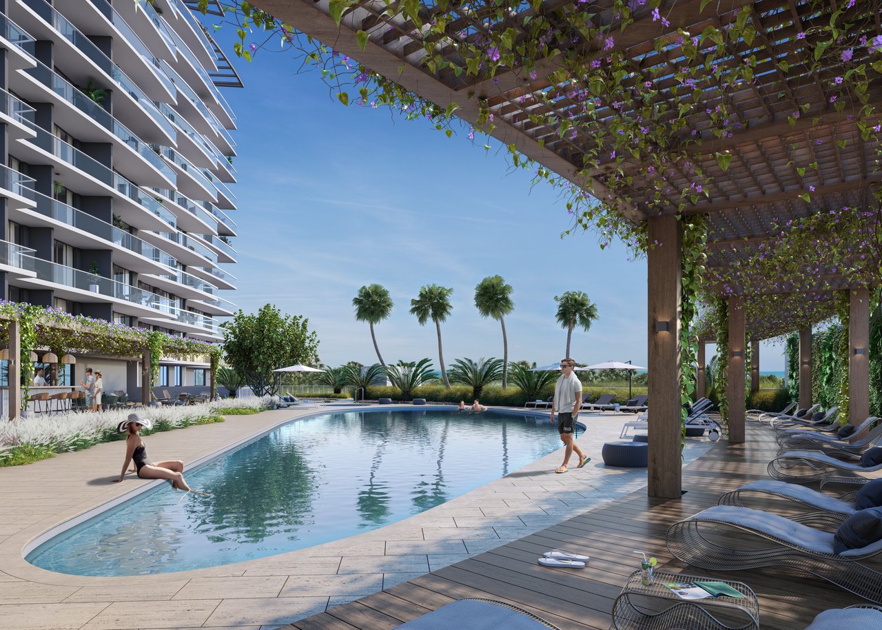 Residential pool deck beside a modern tower, with a vine-covered pergola and ocean glimpse.