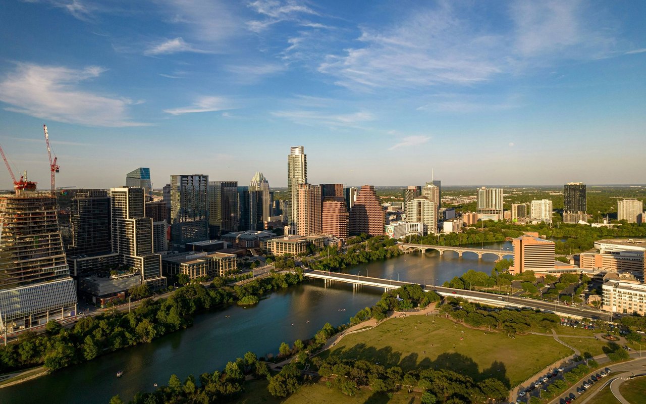 Aerial view of downtown Austin along the Colorado River, with bridges and parkland.