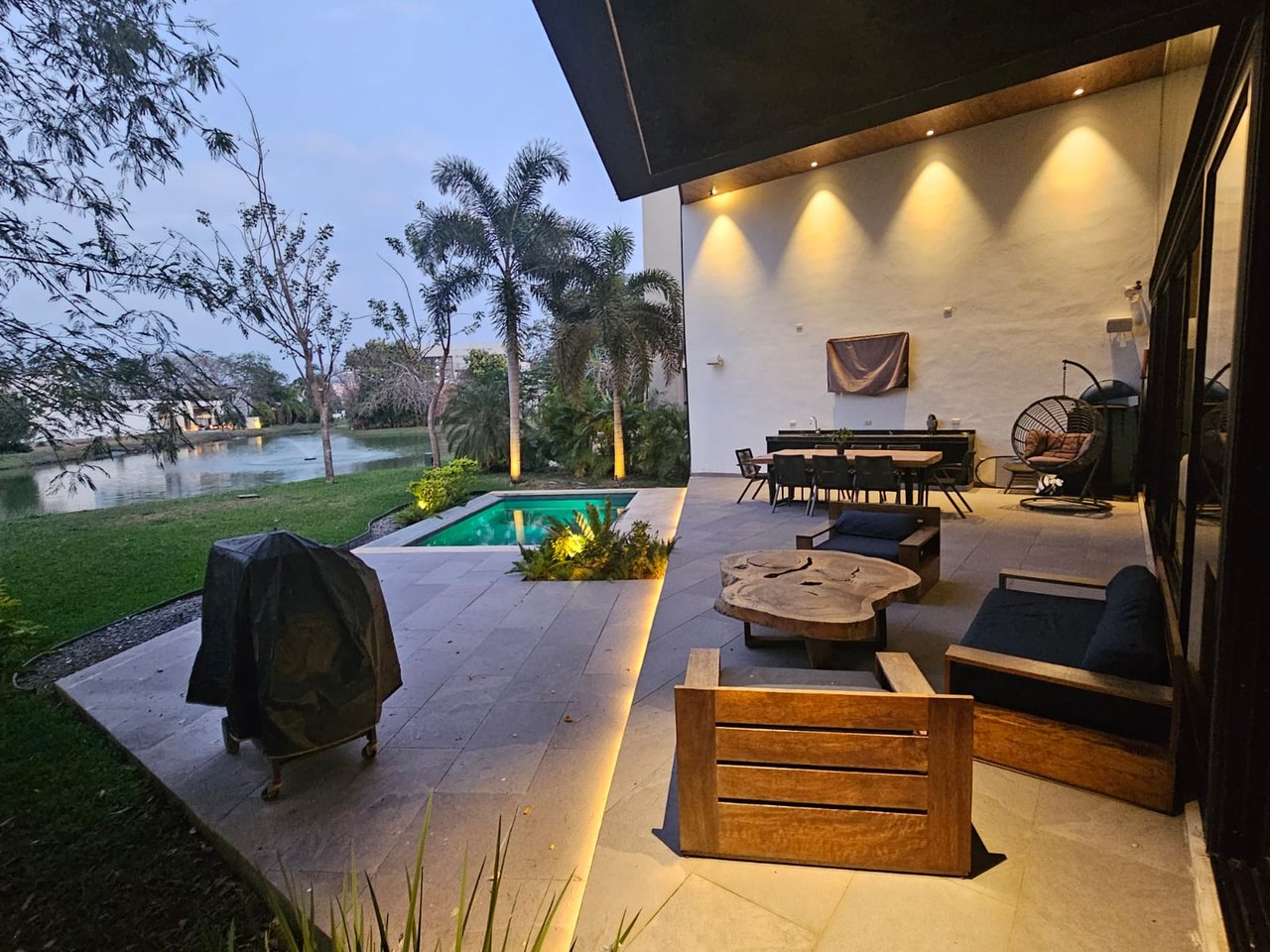 Outdoor patio with poolside lounge seating and dining area overlooking a lake at dusk.