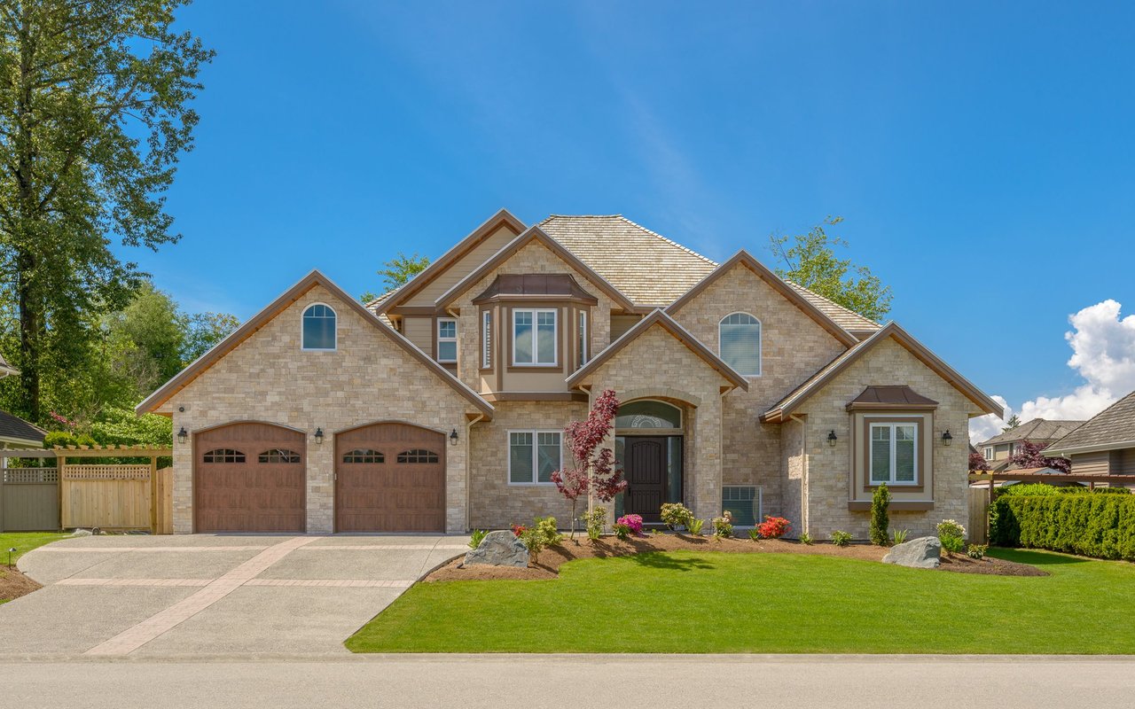 Large stone house with two wooden garage doors and a landscaped front lawn.