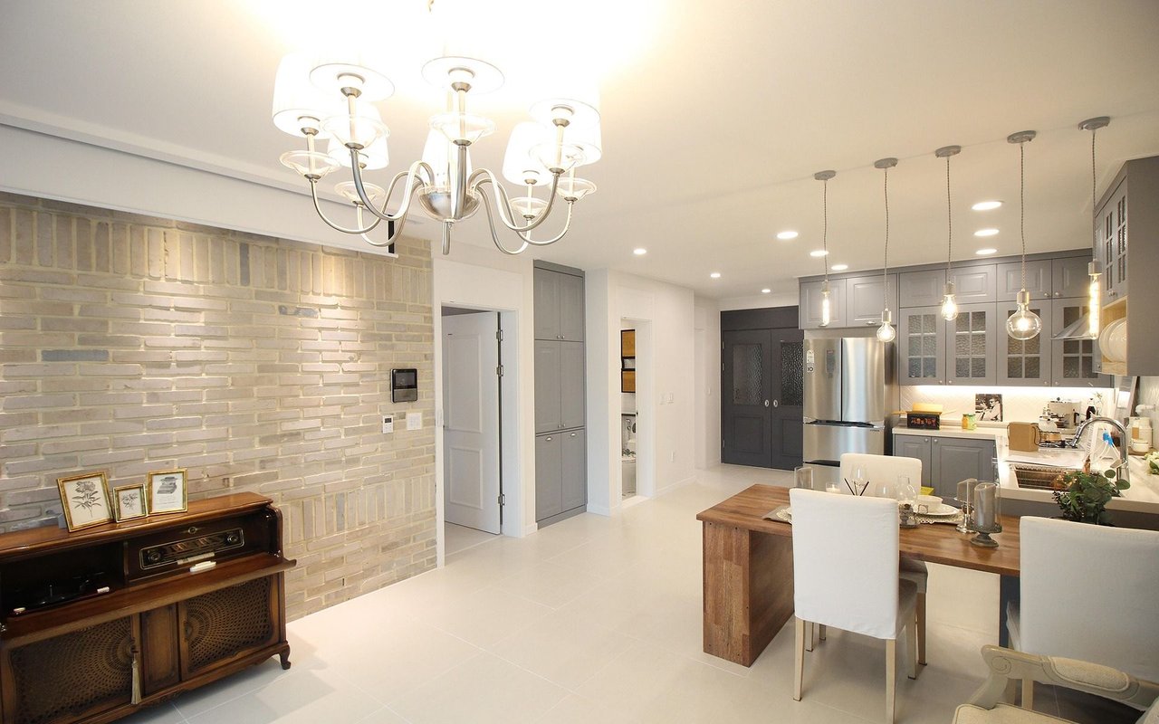 Open-plan kitchen and dining area with gray cabinets, a wood table, and a pale brick accent wall.