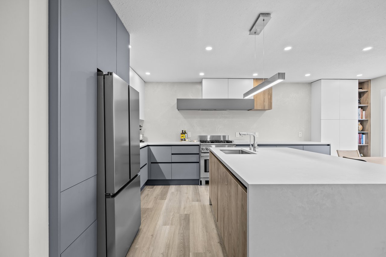 Modern kitchen with gray cabinetry, stainless steel appliances, and a large island with a white countertop.