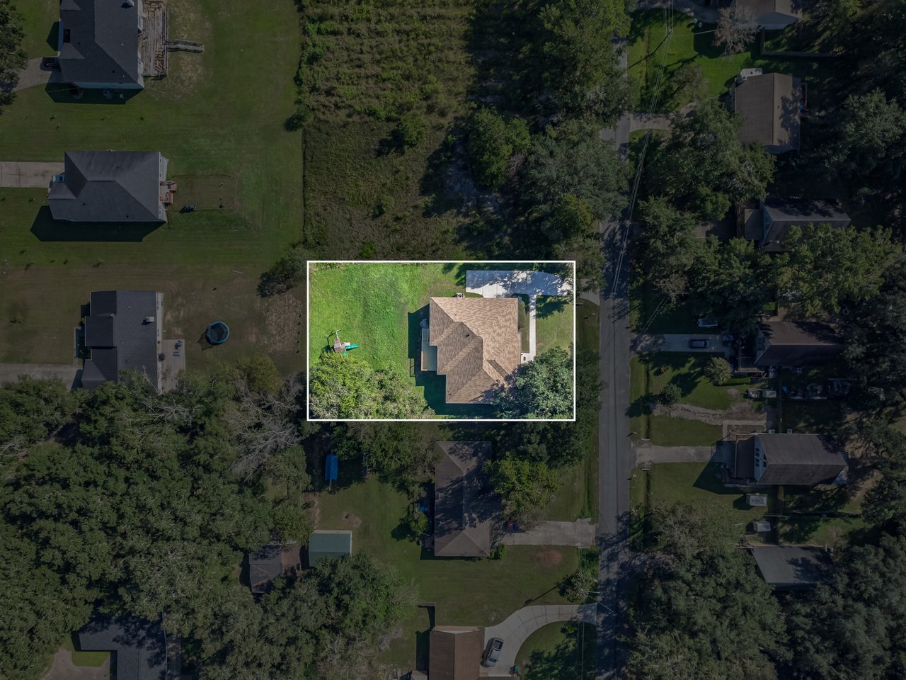 Aerial view of a detached home and yard outlined in white among neighboring homes and trees.