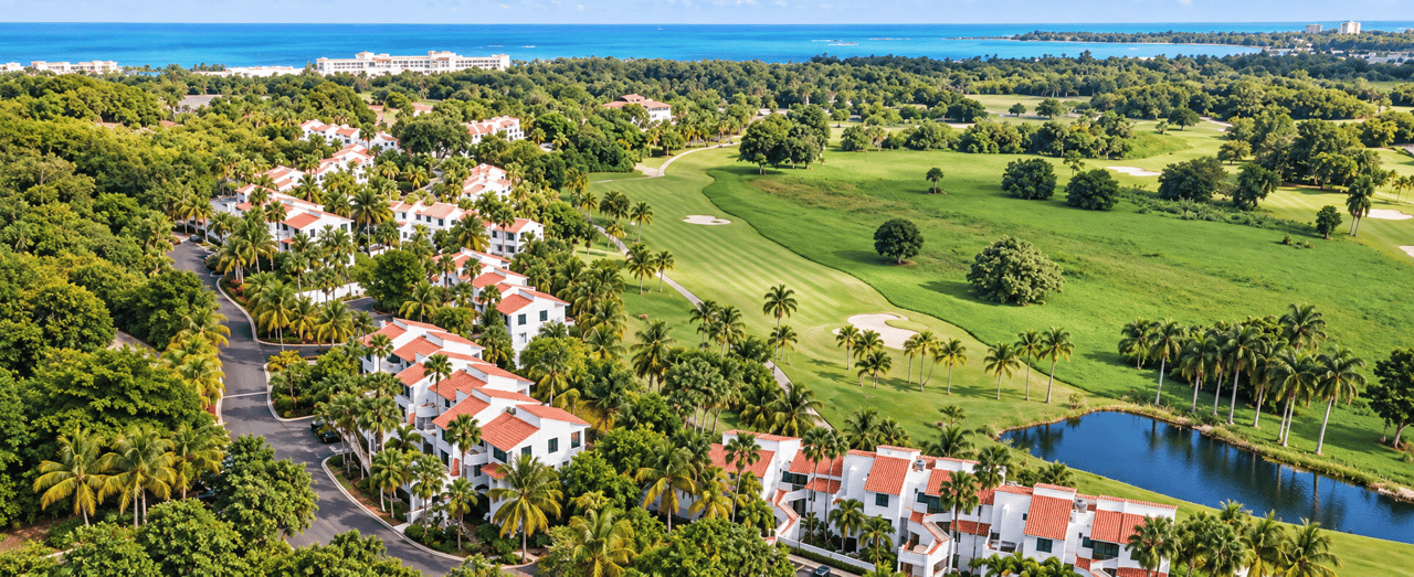 Aerial view of Rio Mar Village condos beside a palm-lined golf course, lake, and Caribbean coast.
