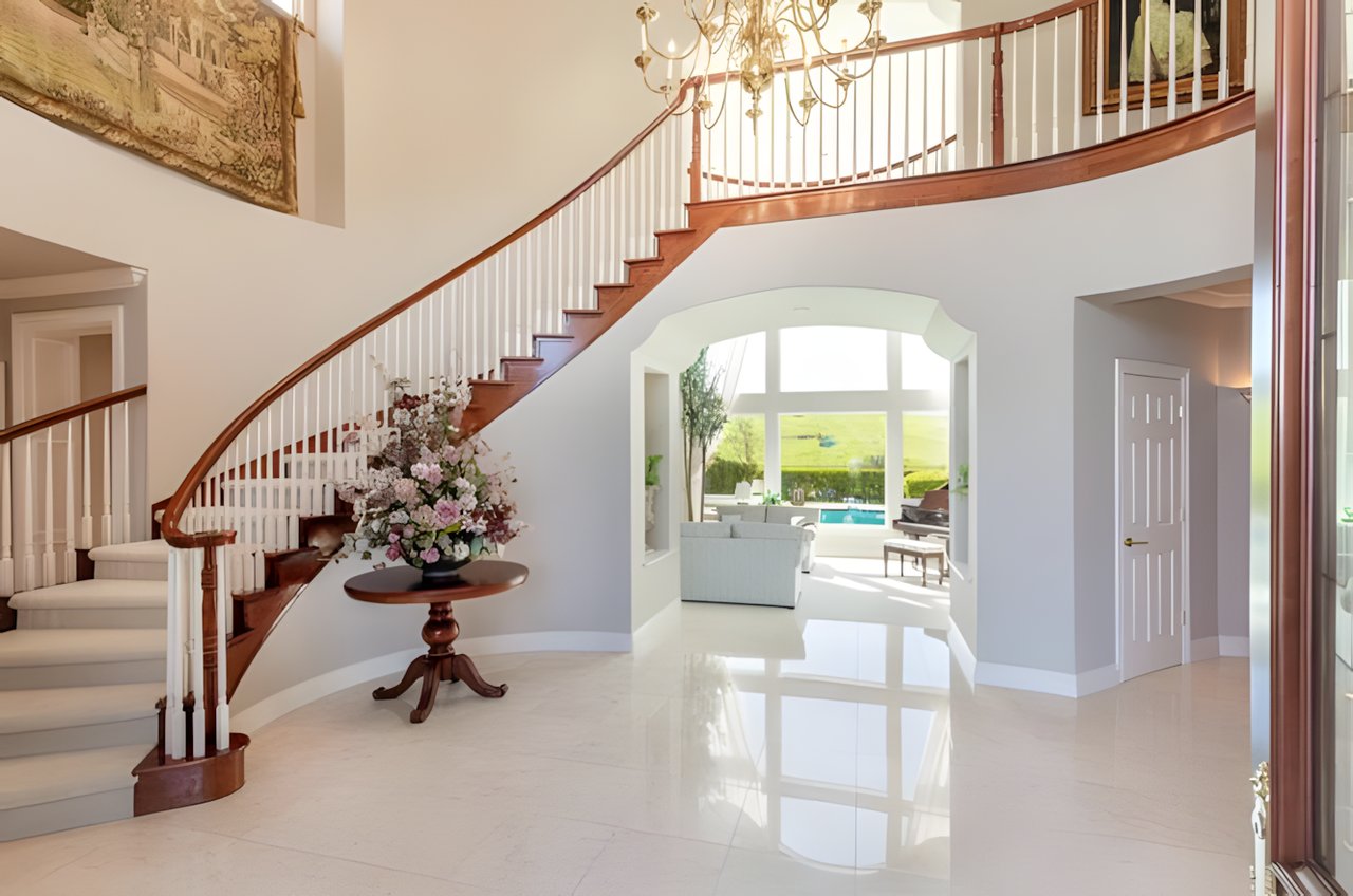 Home foyer with a curved staircase, chandelier, glossy tile floors, and a pool visible through the living room windows.