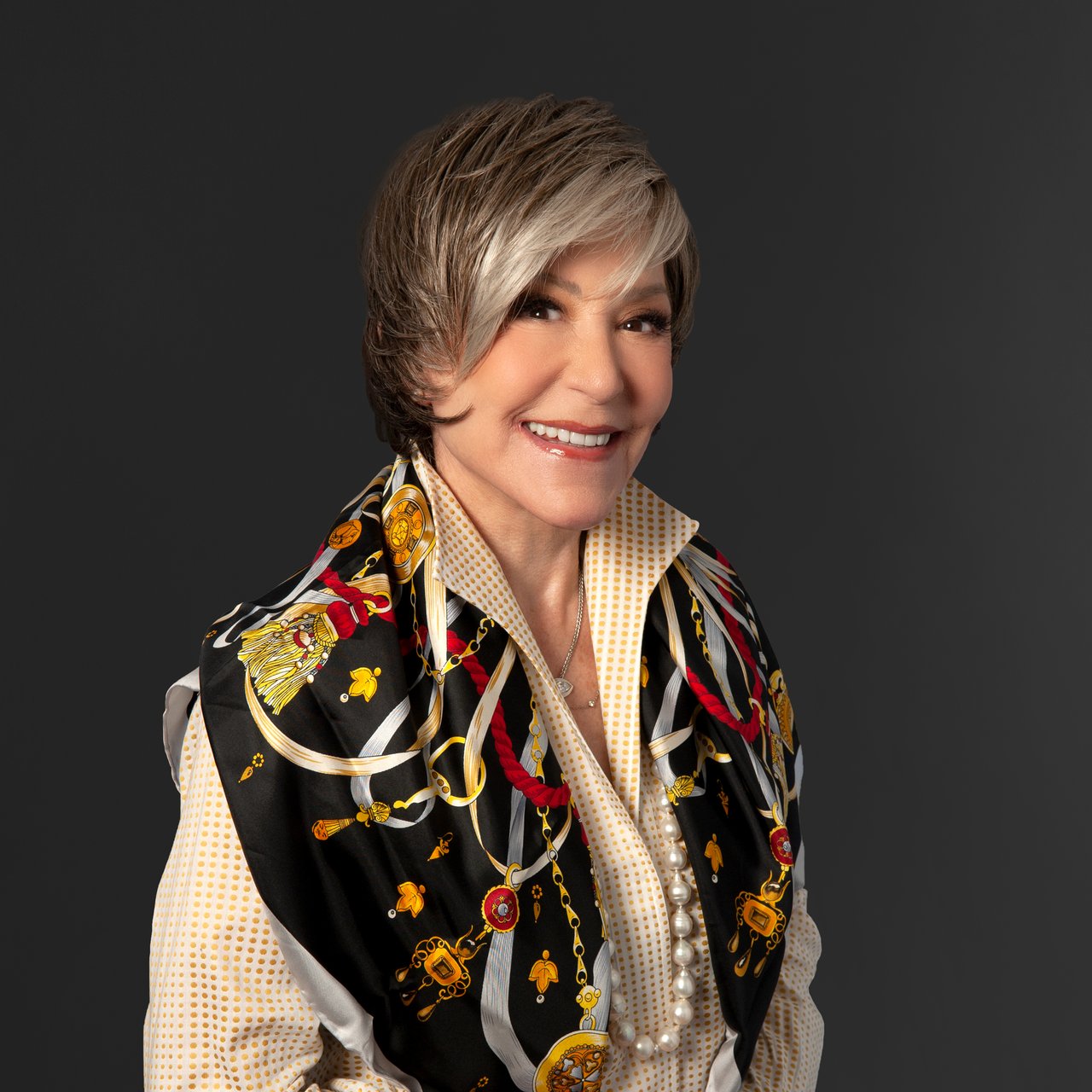 Cynthia Palmer smiling in a patterned silk scarf and white blouse.