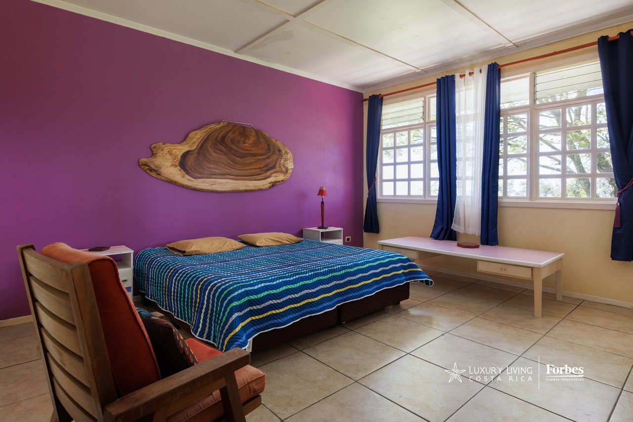 Bedroom with a blue striped bedspread, purple accent wall, and broad windows with blue curtains.