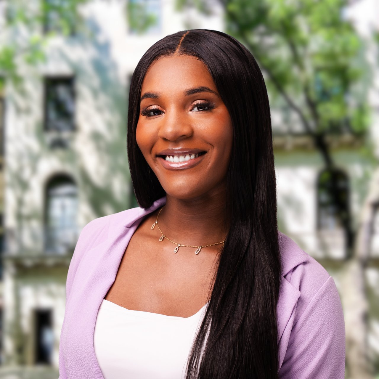 Jasmine Givens smiling in a lavender blazer, with a blurred building and greenery behind her.