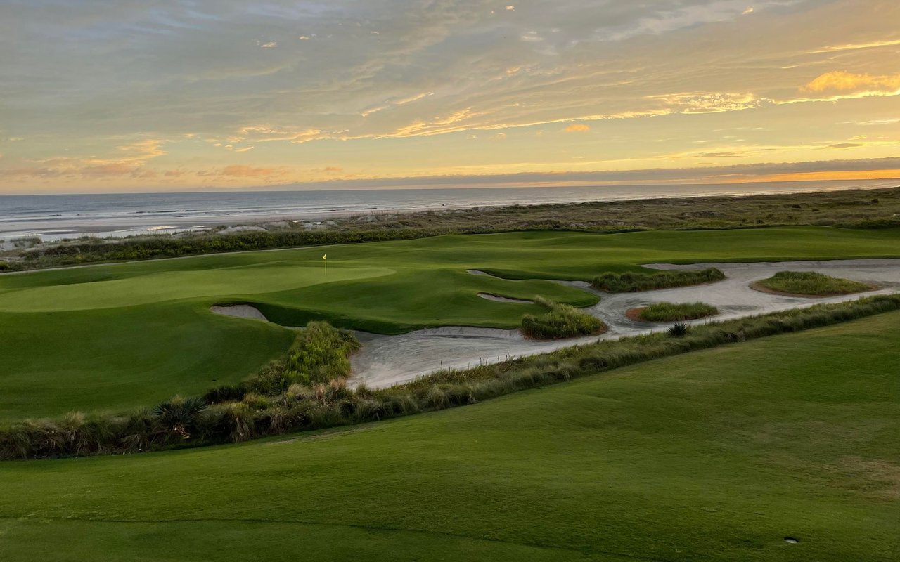 Coastal golf course beside the ocean beneath a golden sunset.
