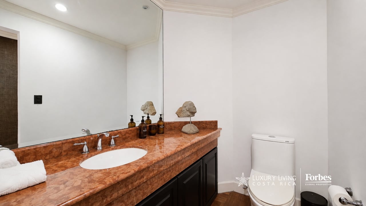 Condominium bathroom with a reddish-brown stone vanity, oval sink, large mirror, and white toilet.