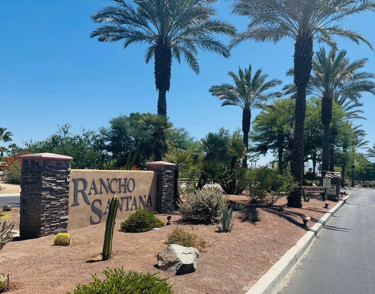 Rancho Santana entrance sign among palm trees and desert landscaping.