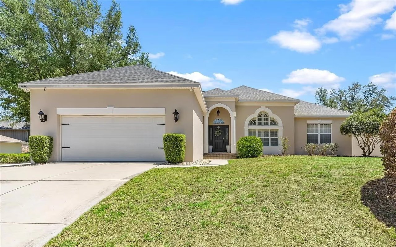 Beige single-story home with a white double garage, arched entry, and broad front lawn.
