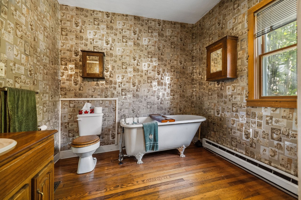 Bathroom with a clawfoot tub, vintage collage wallpaper, and a large wood-framed window.