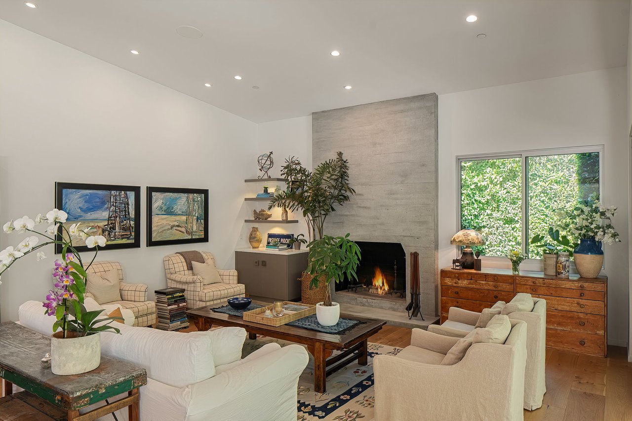 Living room with a tall concrete fireplace, white seating, and a large window facing greenery.