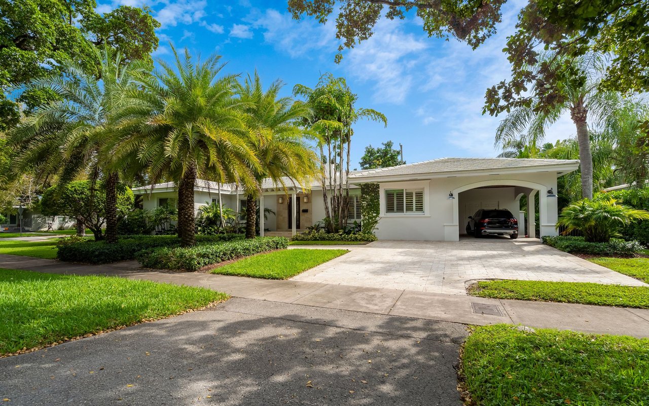 Single-story white home with a wide driveway, attached carport, and mature palms.