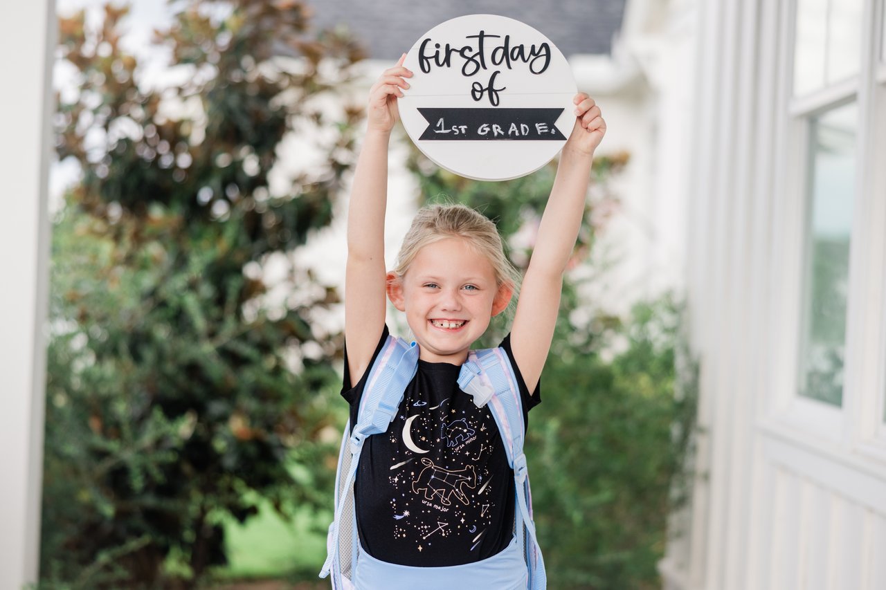 Girl holding first day of first grade sign above her head with a large smile. 