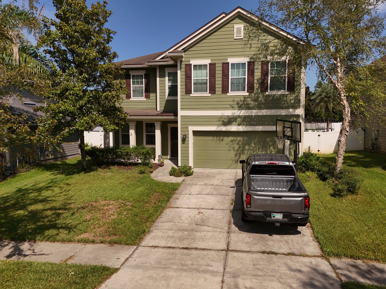 Two-story green home with brown shutters, a double garage, and a pickup truck in the driveway.