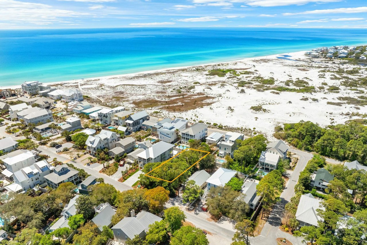 Aerial coastal neighborhood beside turquoise Gulf water, with a wooded lot outlined in orange.