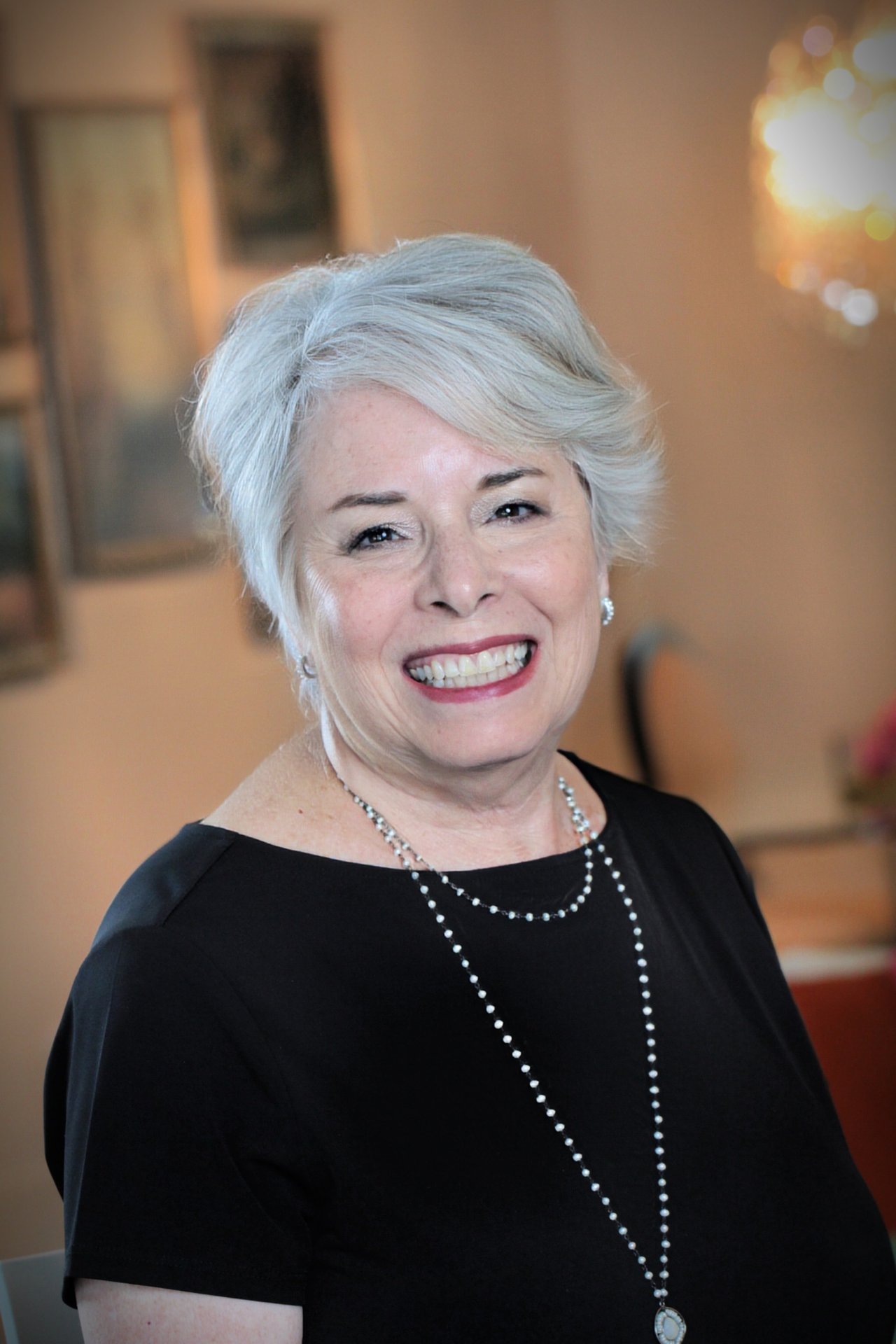 Ann Dee Brahms smiling in a black top and long beaded necklace.