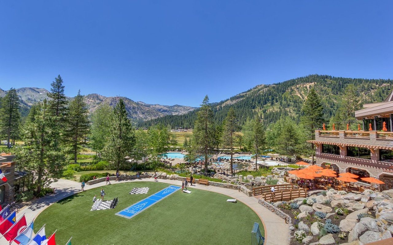 Resort courtyard with a swimming pool and patio seating against a forested mountain backdrop.