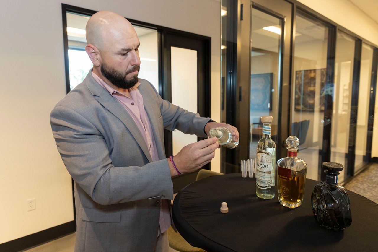 Man in a gray suit pours a liquor sample at an open-house event.