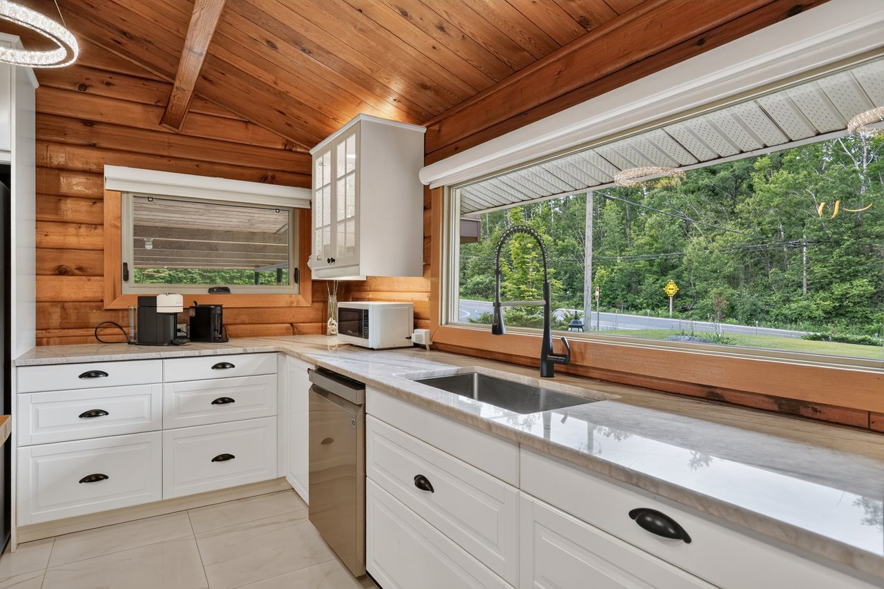 Kitchen with white cabinets, a long sink window, and warm wood walls and ceiling.