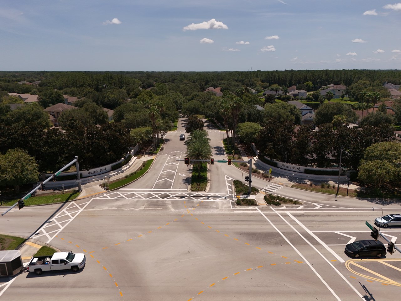 Aerial view of Austin Park’s landscaped entrance and palm-lined road at a signalized intersection.