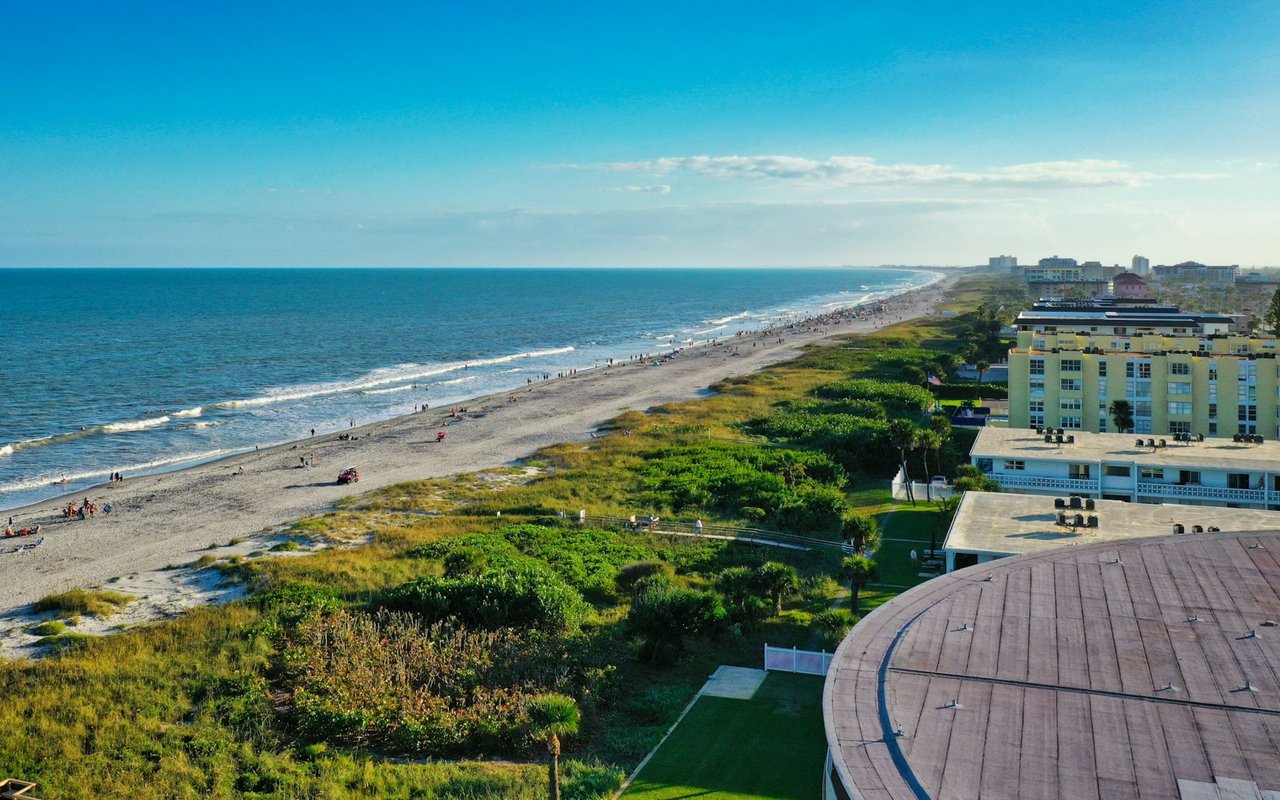 Elevated view of a broad beach, ocean surf, coastal vegetation, and beachfront condominiums.