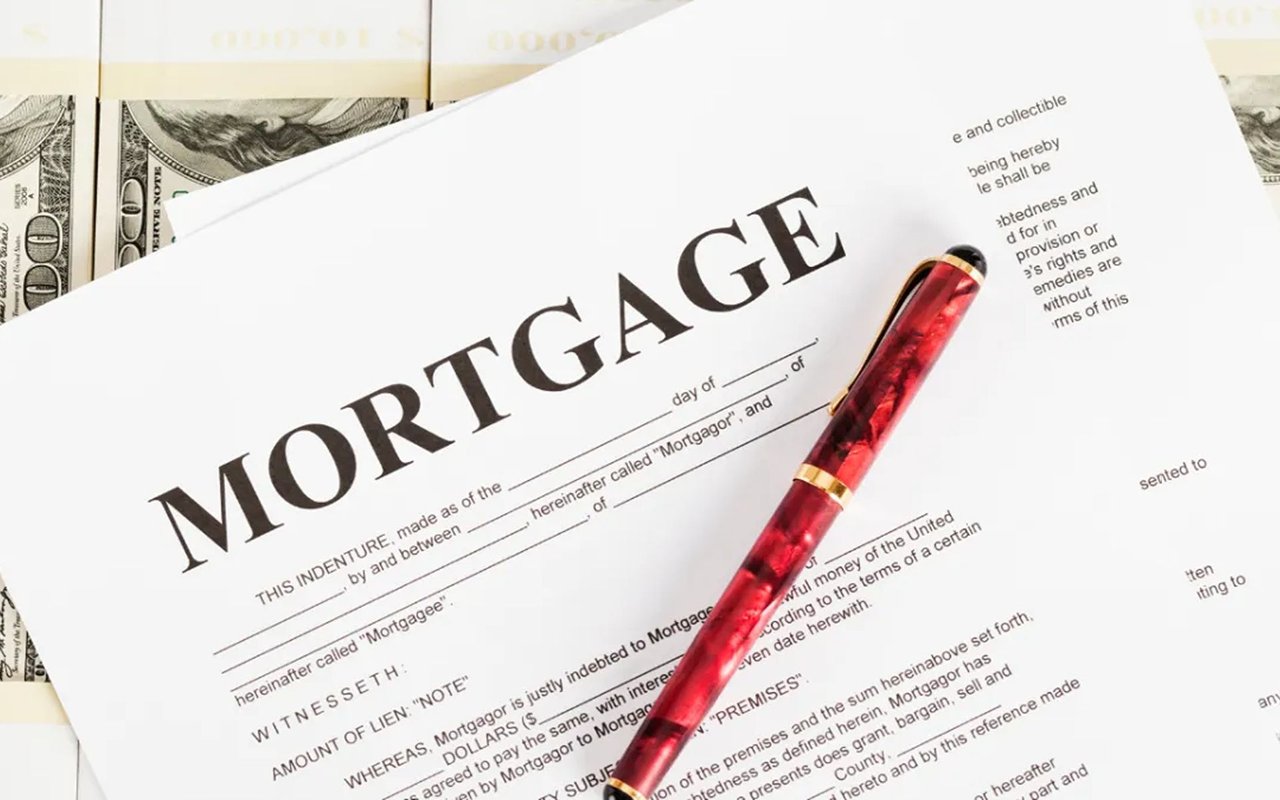Mortgage document with a red pen resting across it and dollar bills underneath.
