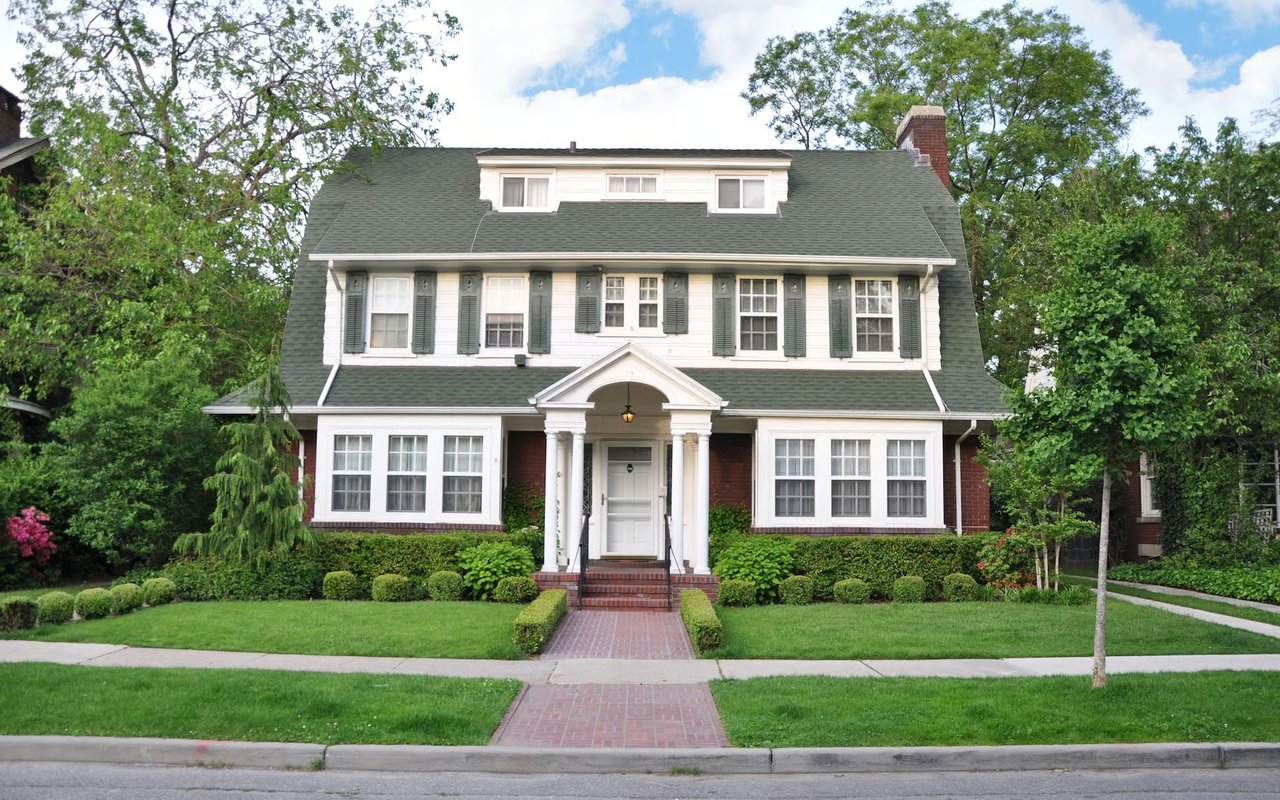 Two-story house with a columned entry, green roof, and brick walkway through a landscaped lawn.