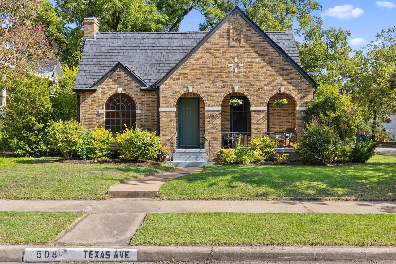 Brick house with a gray shingle roof, arched porch, green front door, and landscaped lawn.
