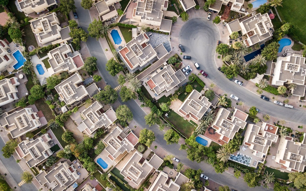 Aerial view of homes with private pools and curving streets in a landscaped community.