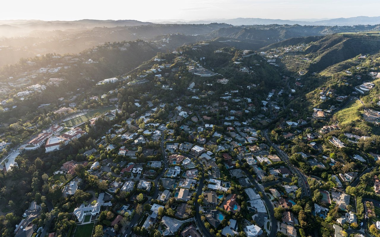 Aerial view of homes and winding roads among tree-covered hills.