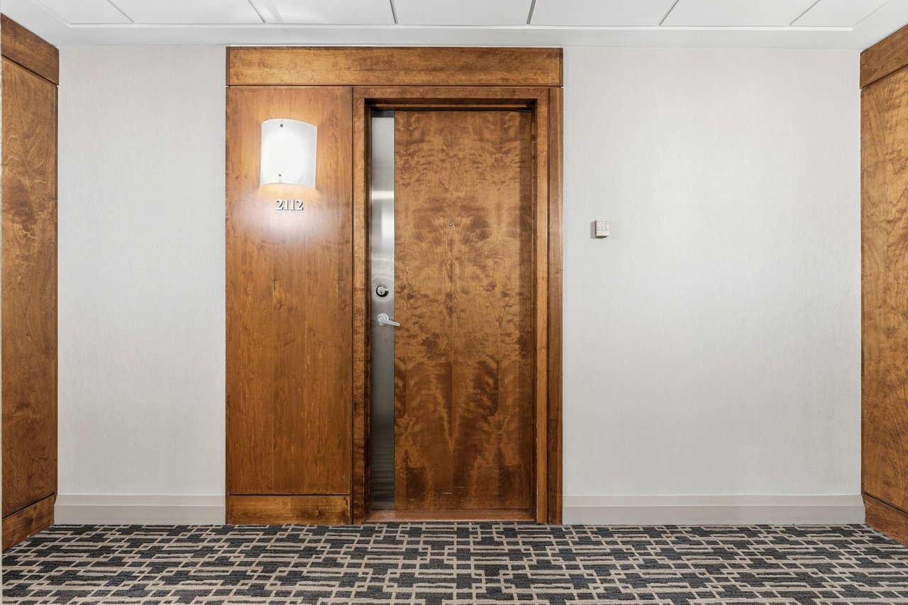 Condominium entrance 2112 with a richly grained wood door and geometric-patterned hallway carpet.