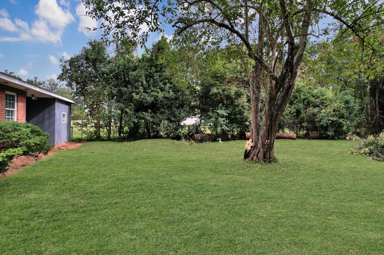 Aerial view of a house surrounded by lush trees and green grass, showcasing a serene residential landscape.